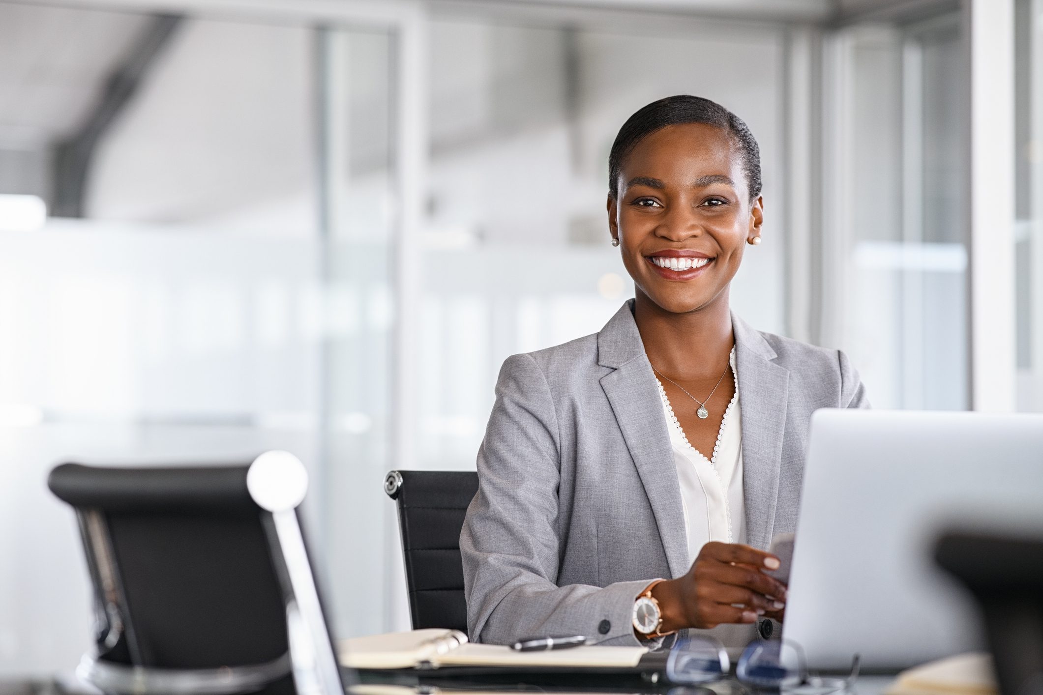 Smiling professional woman in a gray blazer working on a laptop.