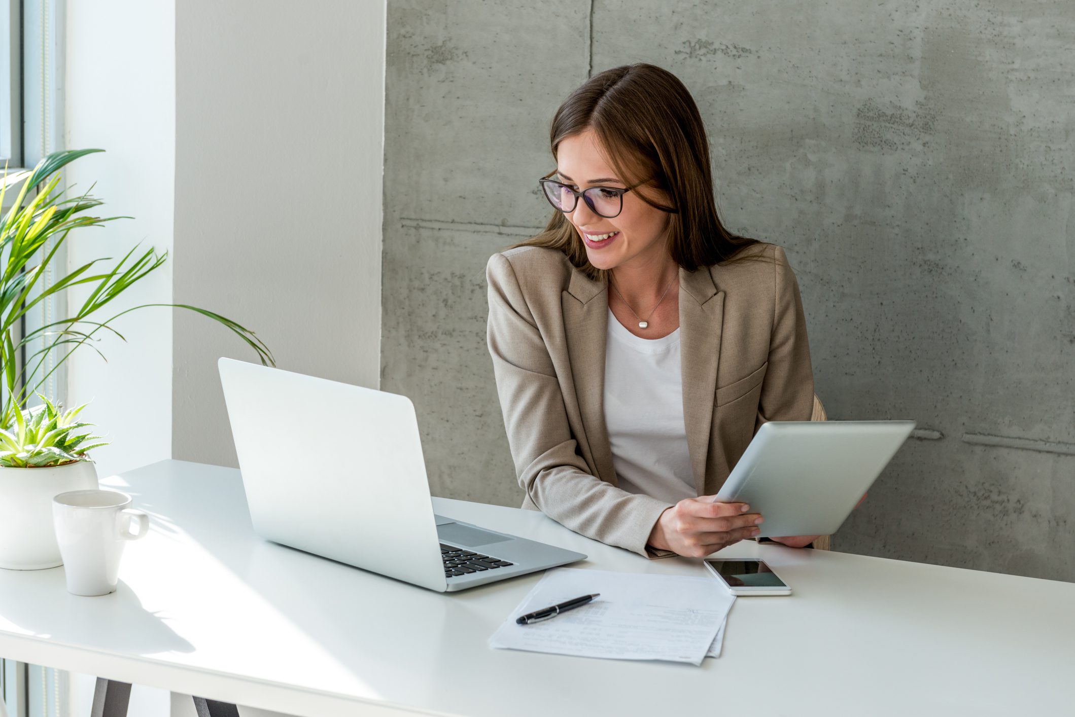Professional woman working on a laptop and tablet at a clean desk.