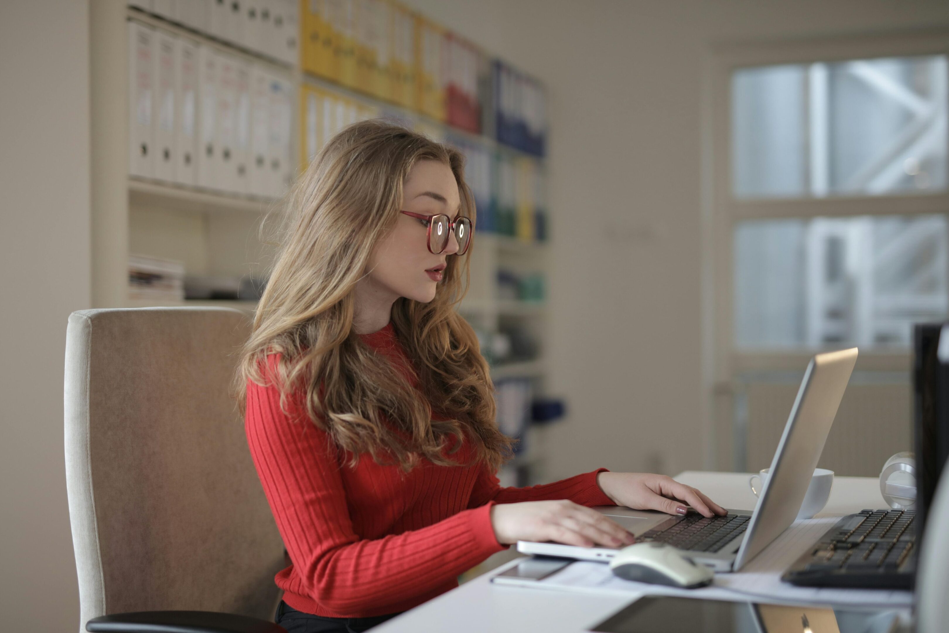 A woman in a red sweater using a laptop at a desk.