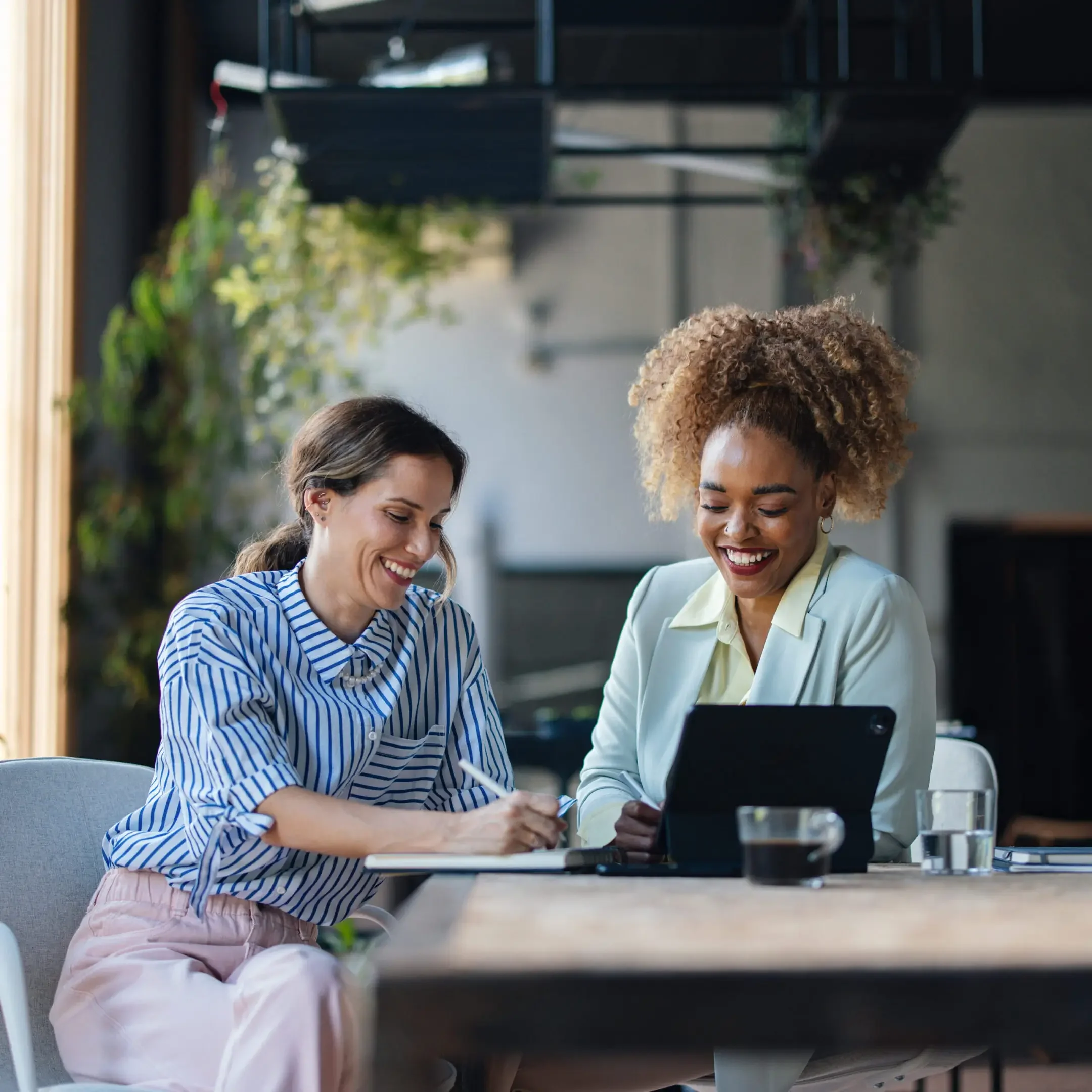 Two women collaborating over a tablet in a cozy cafe.