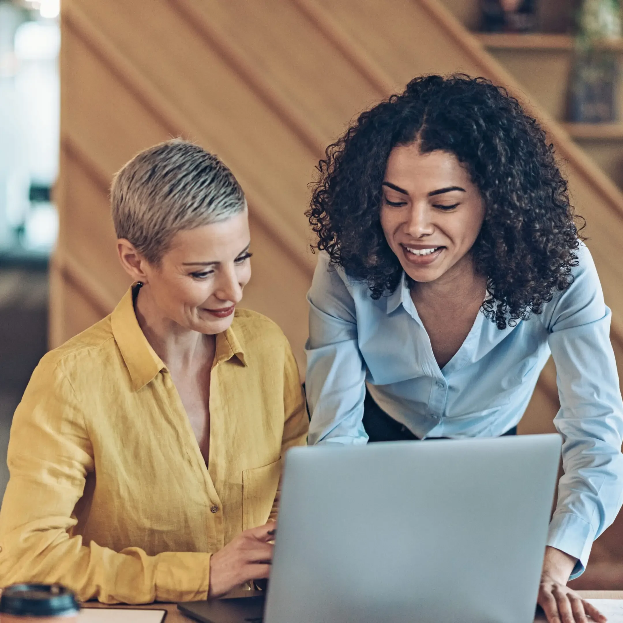 Two women collaborating over a laptop with smiles.